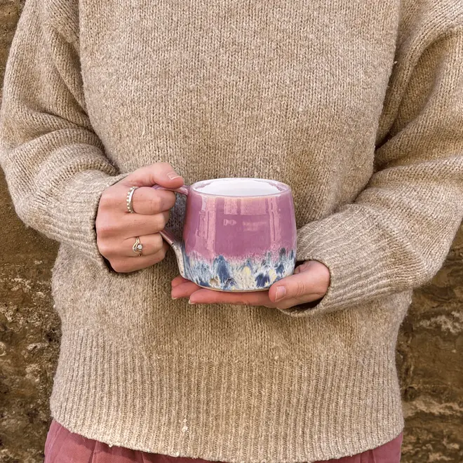 Shoreline Large Round Mug, a woman wearing a jumper holding a colourful mug in her hands in front of her. 