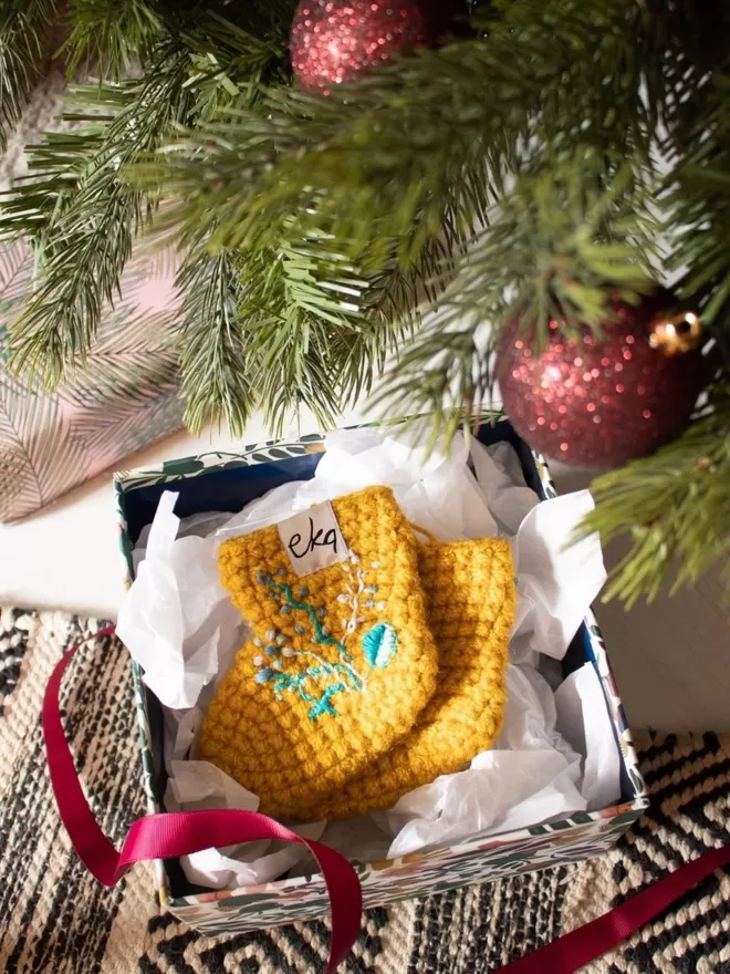 EKA crotched yellow boots with embroidered flowers seen in a box under a Christmas tree.