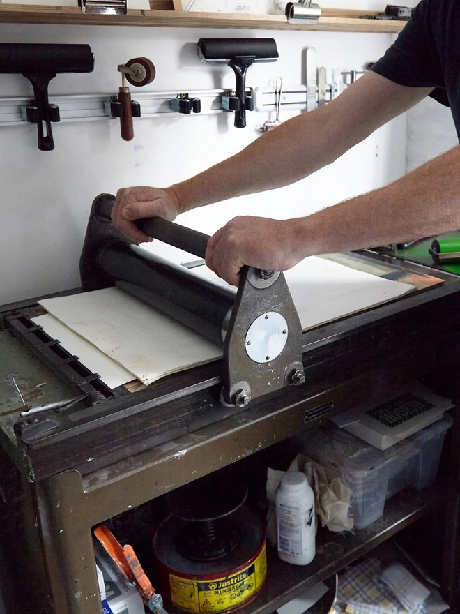 aquarius zodiac linocut. a manual lino press in use.