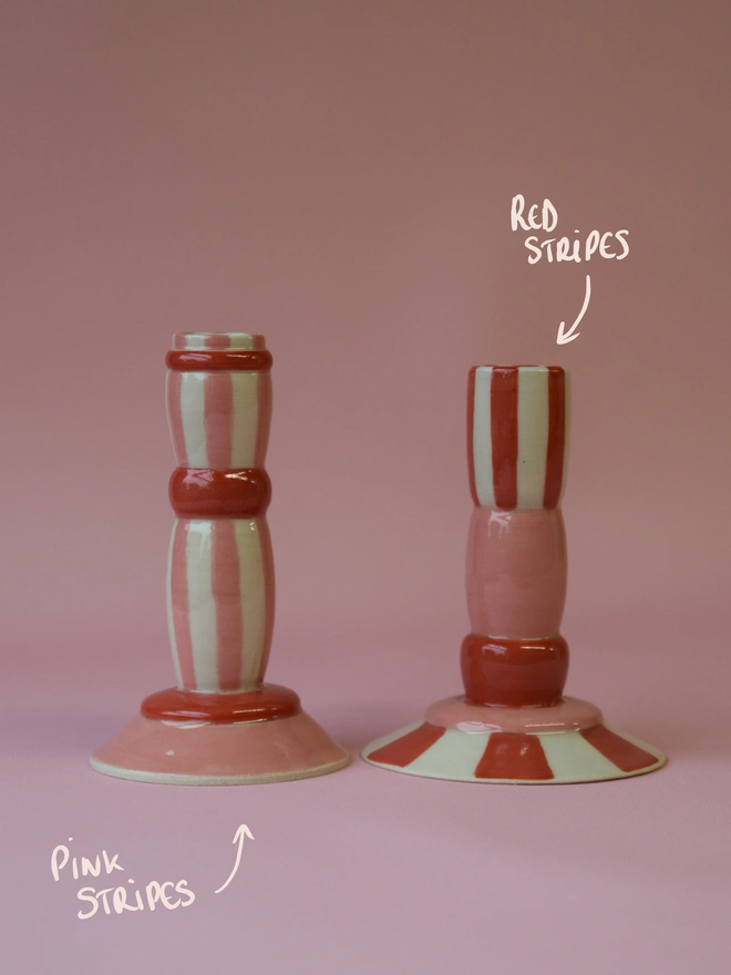 Handmade ceramic candlesticks with pink and red stripe patterns, showing a soft pink striped design on the left and a bold red striped candlestick on the right, styled on a pink backdrop.