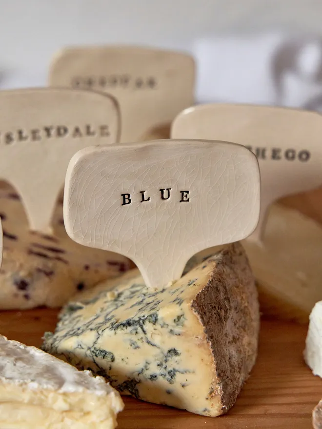 Ceramic cheese marker. That reads Blue placed on a wooden tray