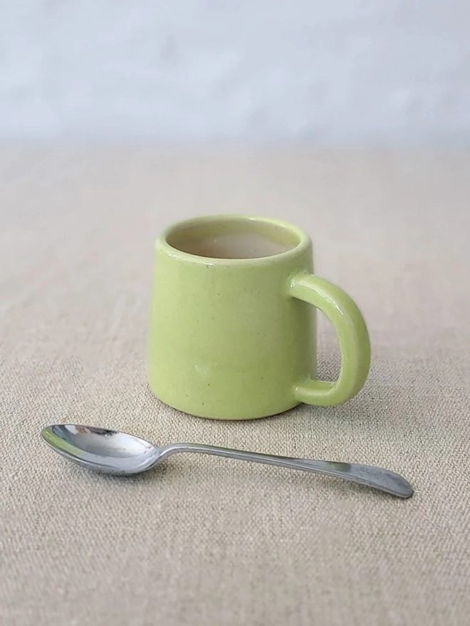 Classic Ceramic Espresso Mug, a colourful ceramic espresso mug sitting on a plain surface against a white backdrop. It is accompanied by a spoon. 