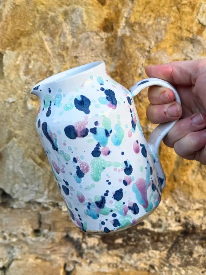 Sweetpea Medium Jug, a colourful jug being poured against a brick backdrop. 
