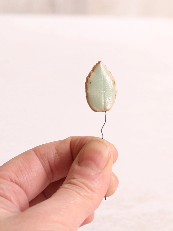 handmade ceramic leave is being held up in front of a white background