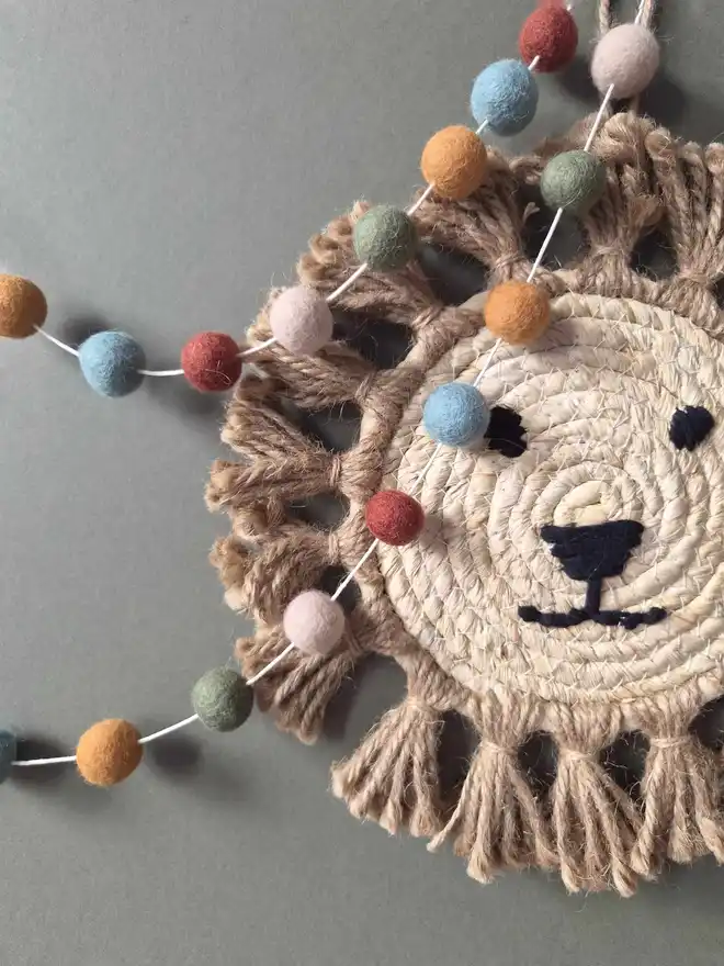 Felt ball garland hanging on a wall with a rattan lion in the background.