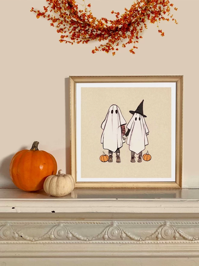 a framed halloween print on a mantle piece of 2 cute children in sheets dress as ghosts