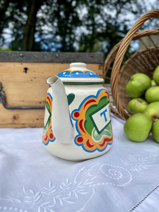 Cream vintage teapot, hand painted with a fairground design in green, blue, yellow and red. ‘Tea’ is painted in a banner across the centre.