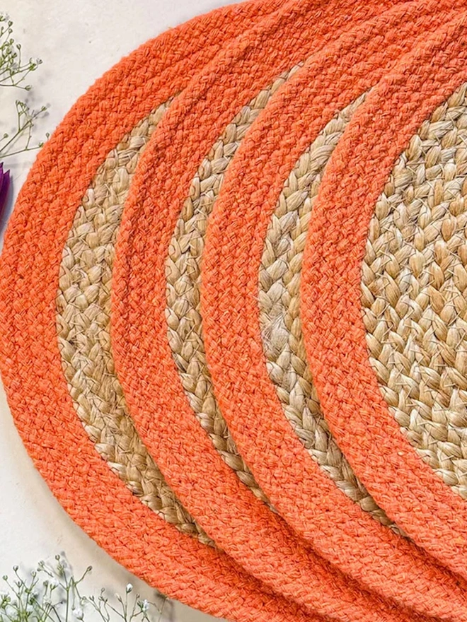 Close up of a round woven seagrass placemats with orange rings, shown on a light surface. 