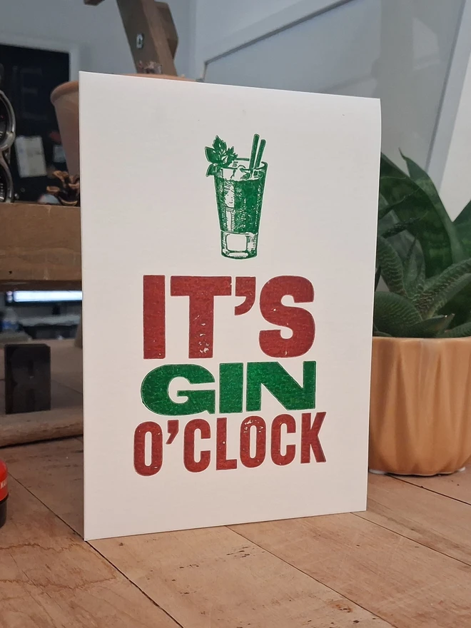 A greetings card printed in burgundy and green with the text 'It's Gin O'Clock'