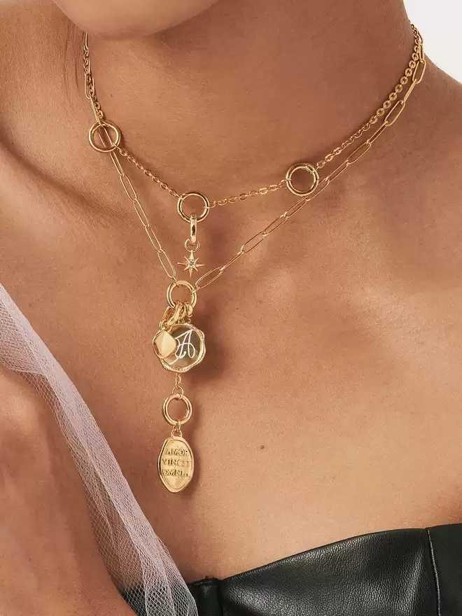 woman wearing two gold necklaces with amor vincit amnia love gold medallion, compass star charm and engravable monogram pendant and charm