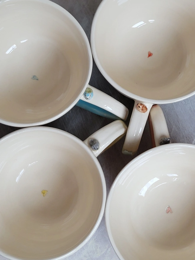 an aerial flat lay shot of glazed handmade pottery cups with robin birds or blue tit on the handle and a handpainted heart inside