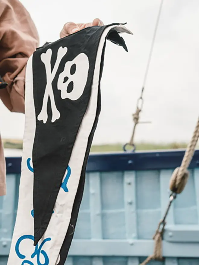 somebody holding up a black pennant flag with an ivory skull and crossbones on.