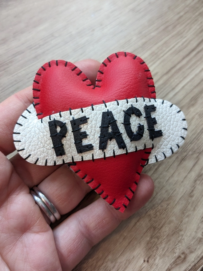 Hetty and Dave red leatherette heart brooch with PEACE in black lettering across a white scroll