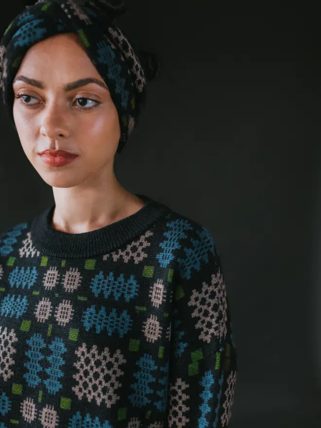 Model wearing pieces from MABLI's 'Carthen' collection, featuring the Carthen Wrap in the vibrant 'Emeralds' colour-way. The design showcases bold, colourful patterns inspired by traditional Welsh blanket tapestry.