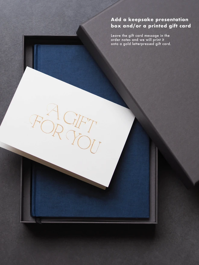 a dark navy book in a dark grey gift box with a gold letter pressed card saying a gift for you