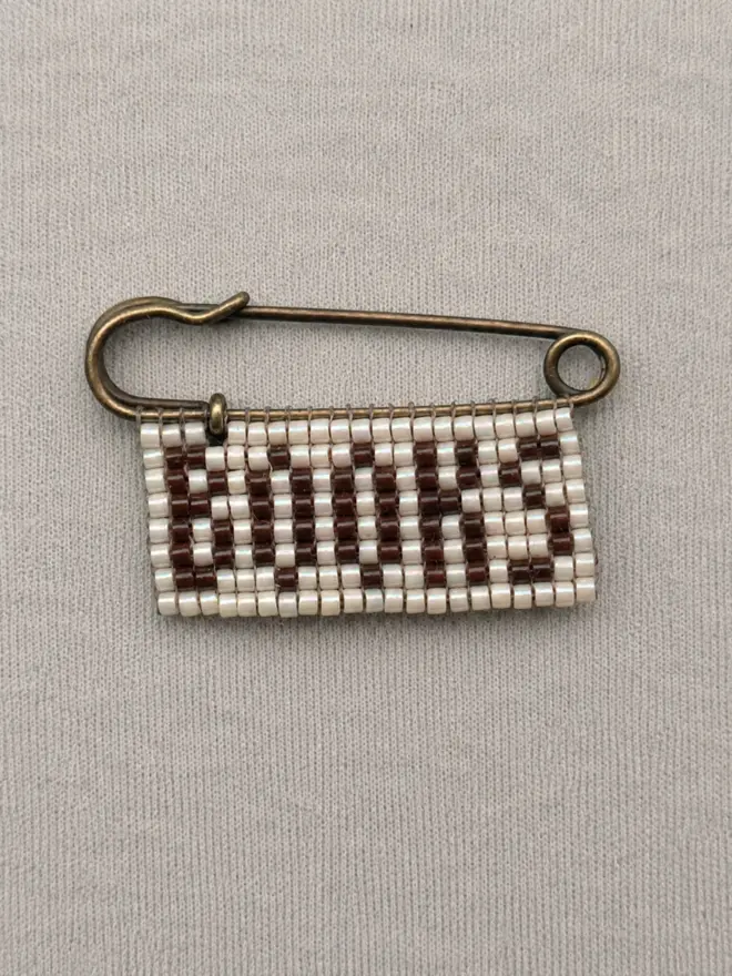 beaded 'books' pin. a beaded pin badge with 'books' in brown letters on a pearl background.