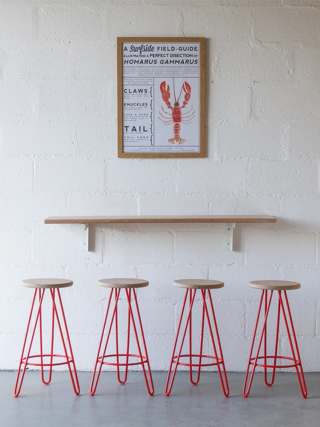 set of four hairpin leg bar stools with red legs and oak seats underneath a red lobster print poster