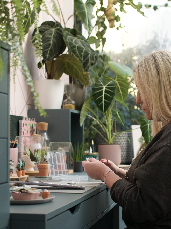 Nicole sat working at her desk making paper plants with real plants in the background