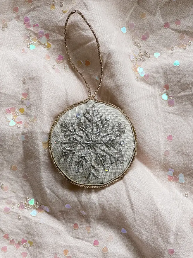 embroidered linen nutcracker snowflake decoration. beaded snowflake hanging ornament photographed on pale pink fabric background.