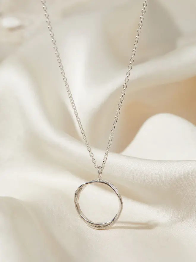 Dainty Sterling Silver Open Circle Necklace draped over silk material