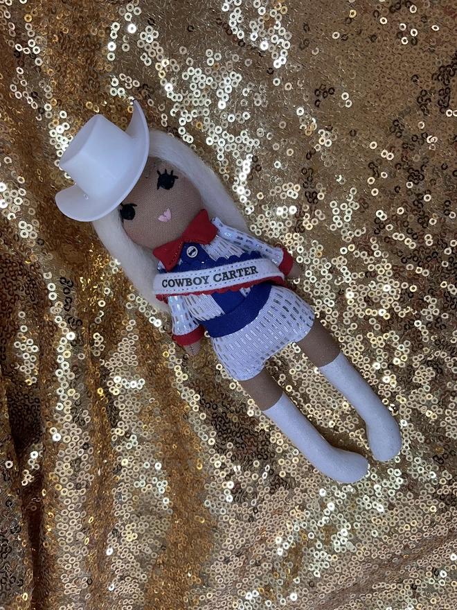 Small decorative fabric doll dressed like Beyoncé in her Cowboy Carter era. Red white and blue outfit.