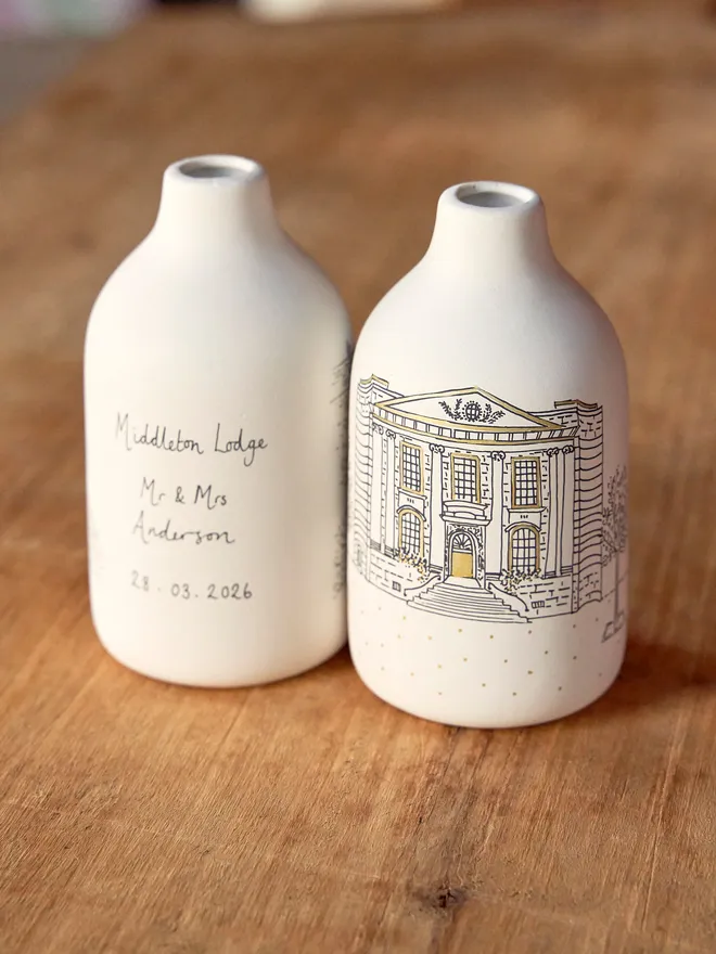 A pair of personalised and hand drawn wedding venue vases on a wooden surface