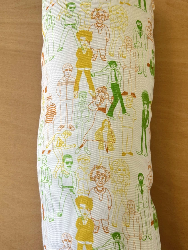 The back of a cushion featuring a design of celebrities in yellow, green and orange on white fabric. 