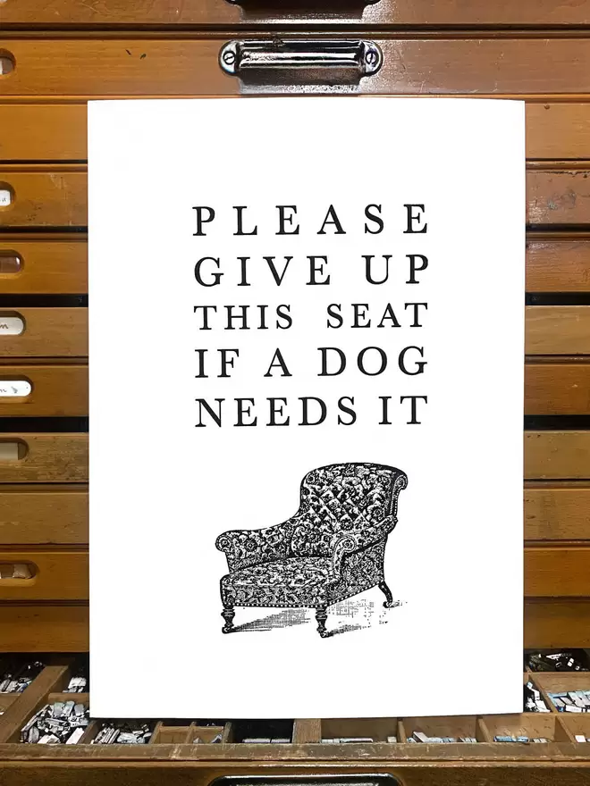 A black and white print with text reading 'please give up this seat if a dog needs it' and an illustration of a chair.