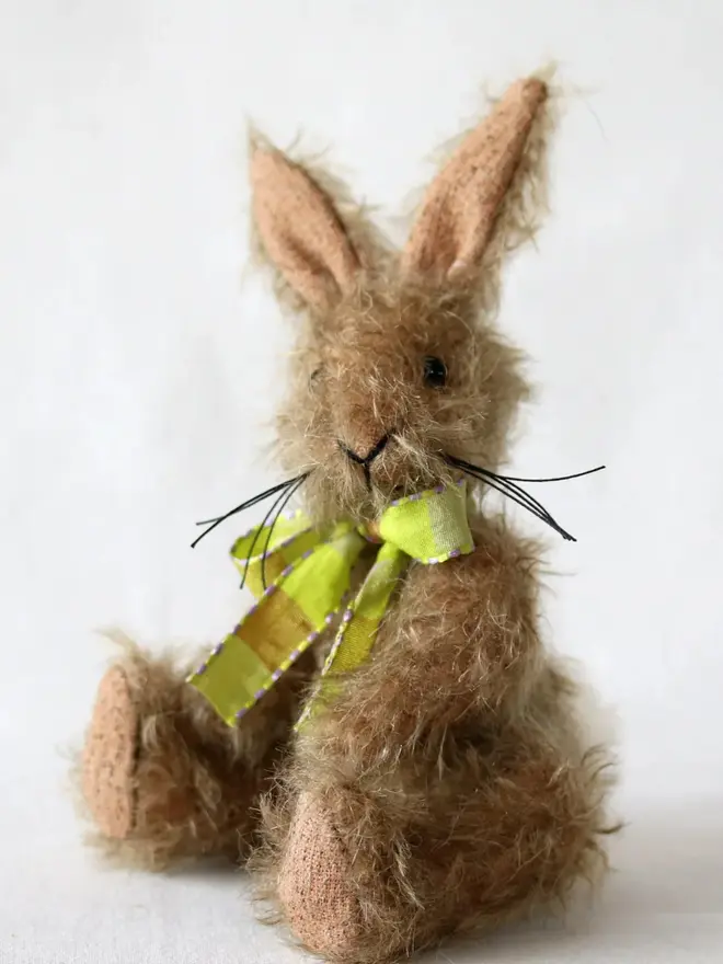 Handmade brown stuffed rabbit with long ears and a green ribbon bow sitting upright against a plain background.