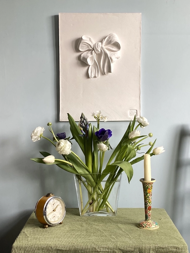 Plaster bas-relief wall plaque with bow and ribbon design with a vase of flowers underneath