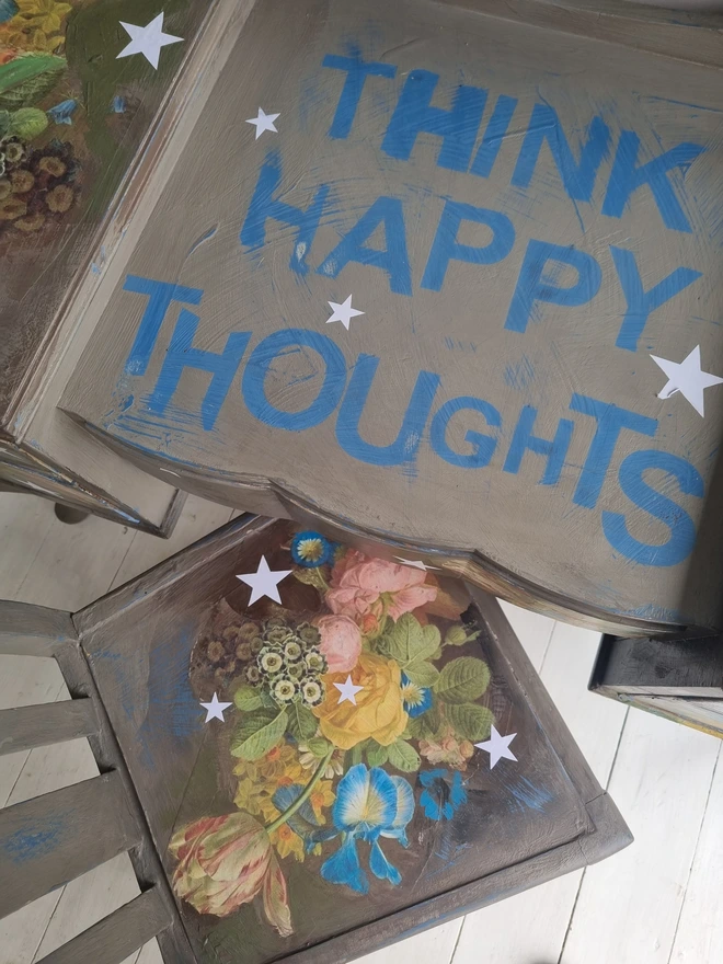 Vintage painted dressing table and chair. Painted in coffee grey and decorated using layered antique florals with yellow and blue accents and finished with hand-cut white paper stars. Text reads in blue 'think happy thoughts'. Heavily distressed finish.