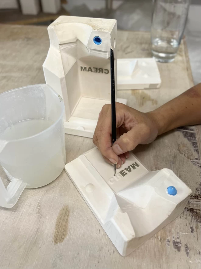 Katie is painting the raised letters spelling cream on the inside of the plaster mould.