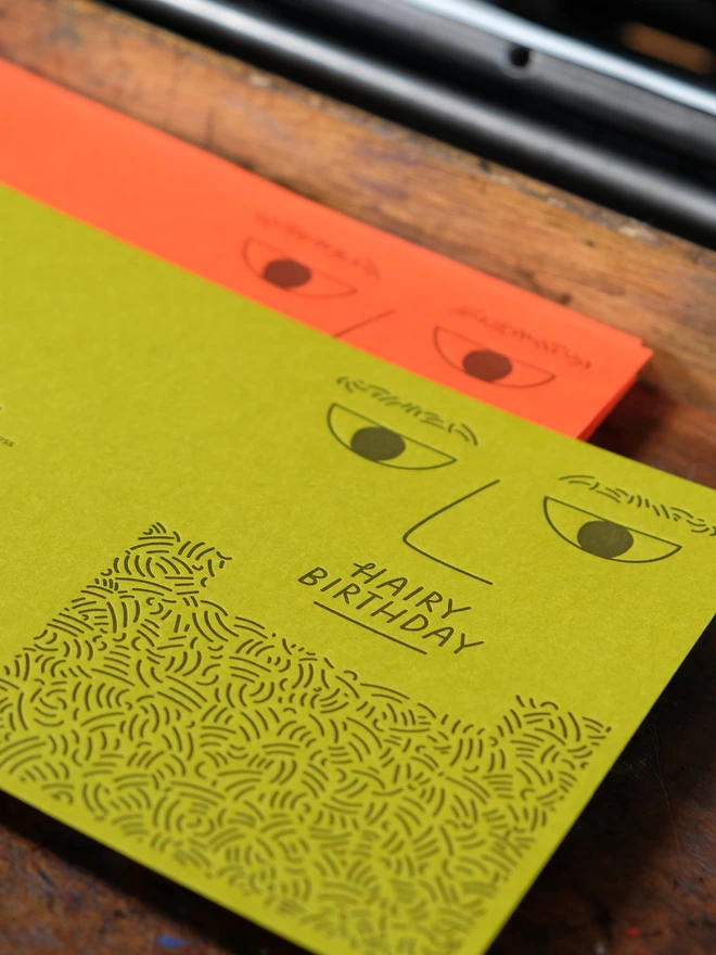 'Kiwi' and 'Tangerine' letterpress 'Hairy Birthday' cards on wooden shelf.