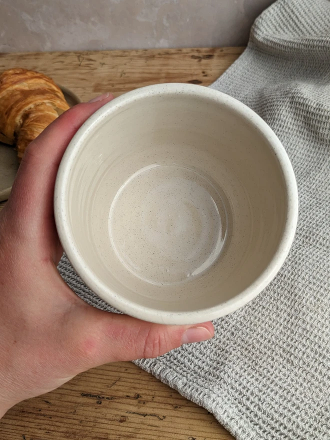 A small white plant pot with croissant design, holding a green leafy plant on a wooden surface.