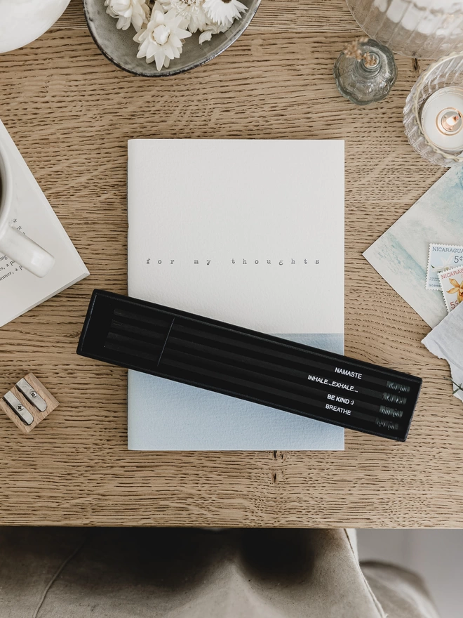 grey and white journal on a desk with some pencils