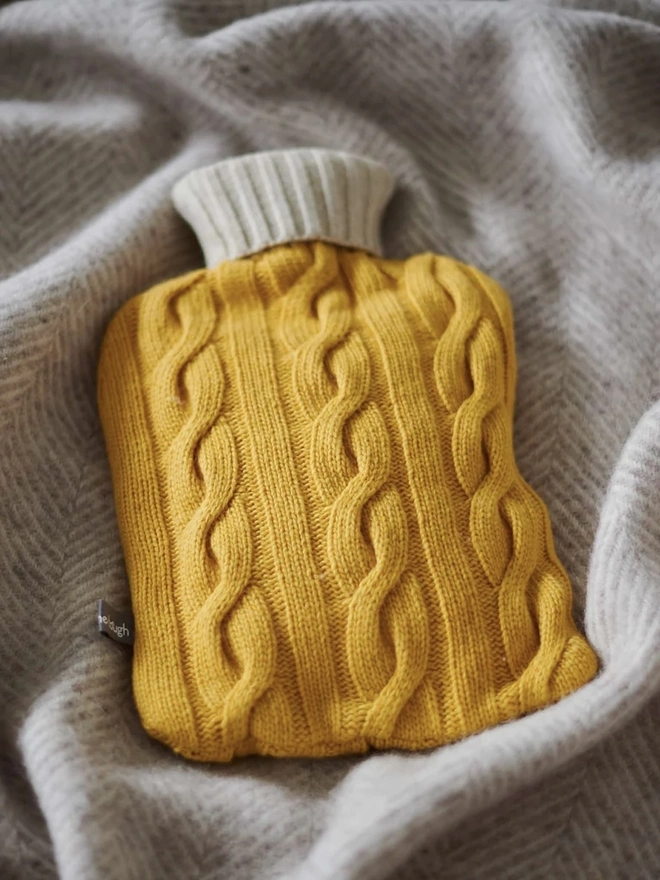 Cashmere Hot Water Bottle Cover, a colourful water bottle sitting on a blanket. 