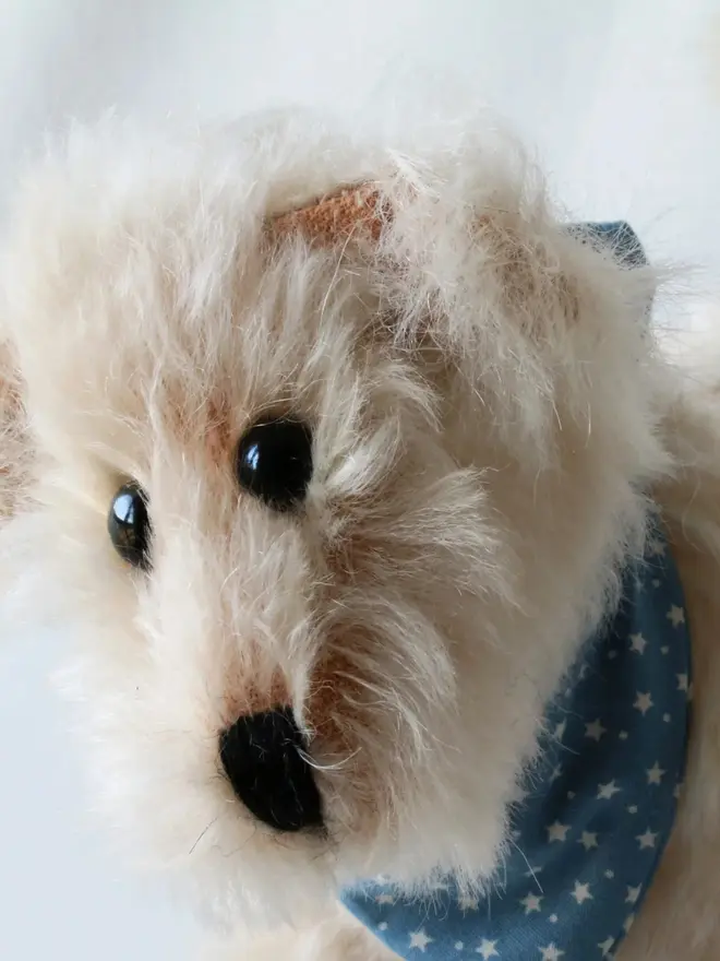 Handmade cream-colored teddy dog wearing a blue bandana standing against a plain background.