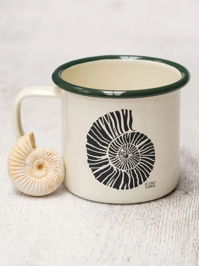 Picture of a Cream Enamel Mug with a Green Rim with a Ammonite design etched onto it, taken from an original Lino Print