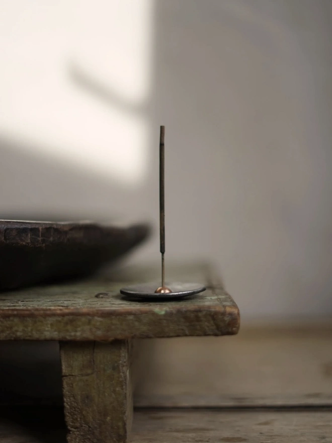 Copper And Steel Incense Holder, a metal incense holder sitting on a wooden surface in a workshop. 