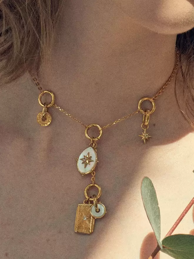 Woman wearing a gold necklace styled with a mother of pearl compass medallion, a starburst pendant and a mix of gold charms