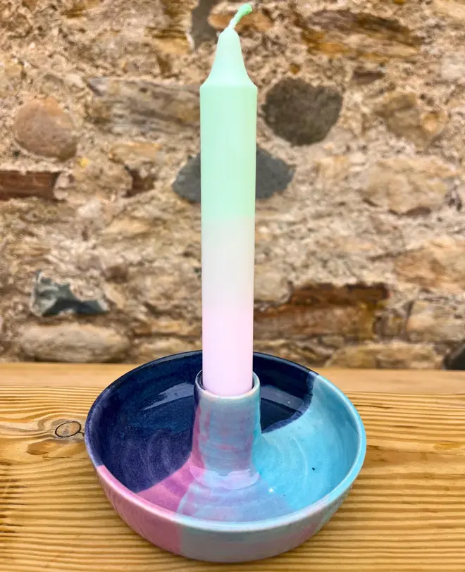 Landscape Candle Stick Holder, a colourful candle stick holder accompanied by a candle sitting on a wooden surface against a brick backdrop. 