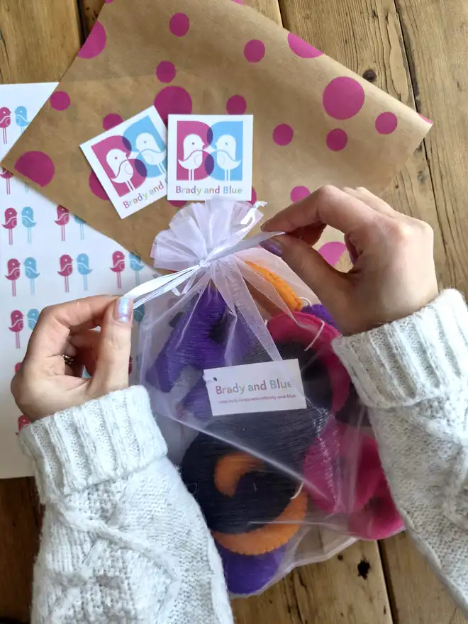 An organza bag laid on top of wrapping paper and stickers. Filled with a bright 'Hocus Pocus' felt Halloween banner. 