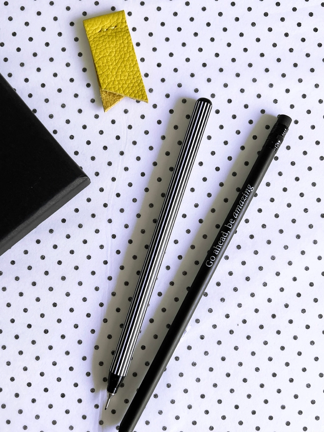 Yellow page marker, striped fineliner, black pencil and notebook corner from stationery gift set on dotted background