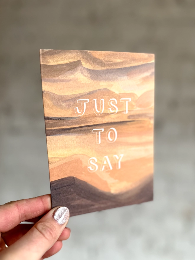 a greetings card featuring an illustration of a sand dunes landscape with the text “just to say”