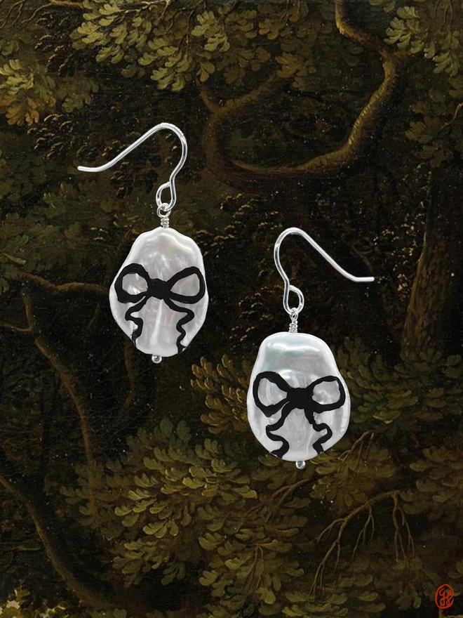 A pair of flat pear shaped pearl drop earrings set in sterling silver with black bow motif painted on the front.