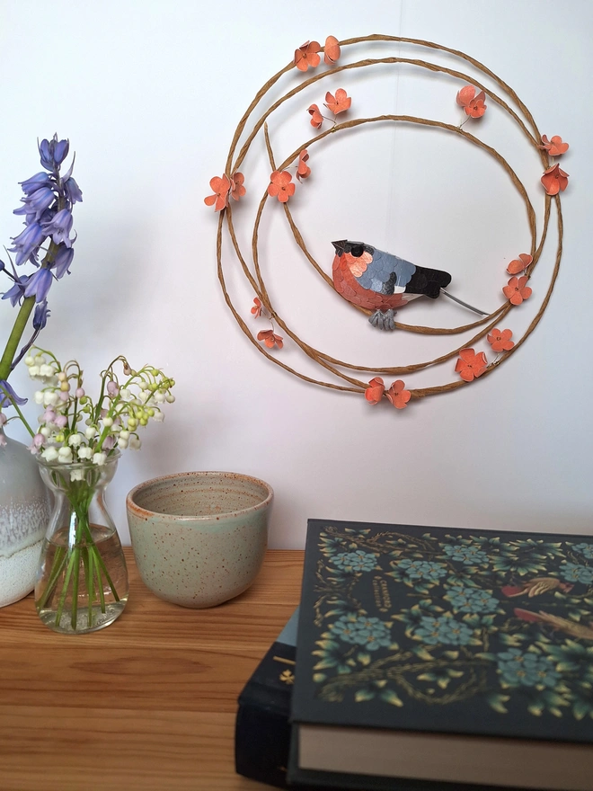 Handmade wall art featuring a bullfinch bird sculpture perched on a wreath adorned with peach blossom
