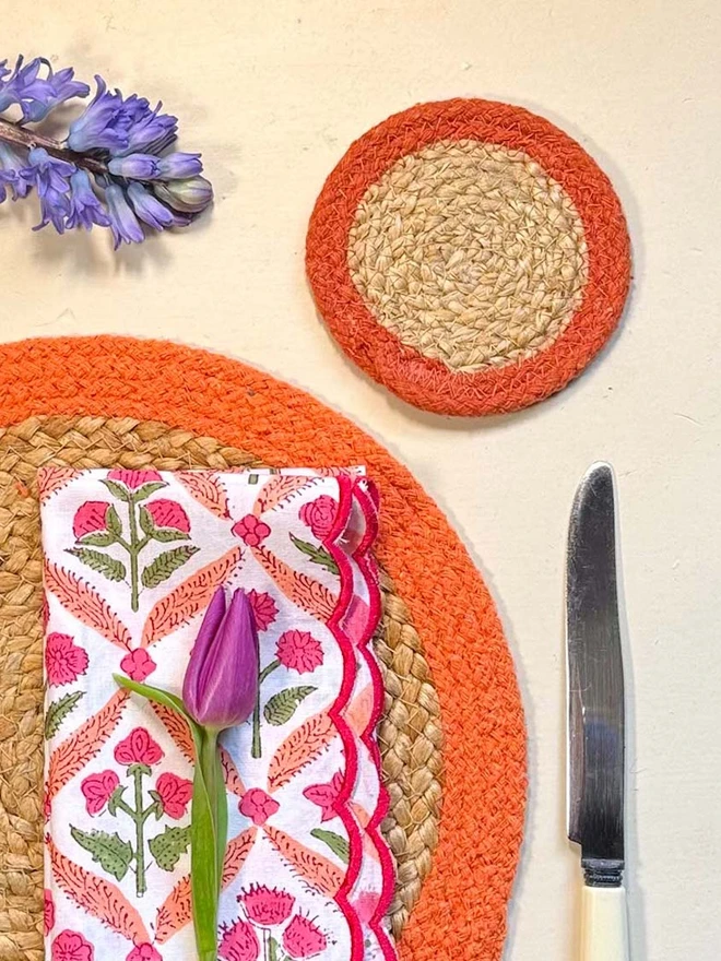 Seagrass coaster with orange rings, shown on a light surface with blue flowers. 