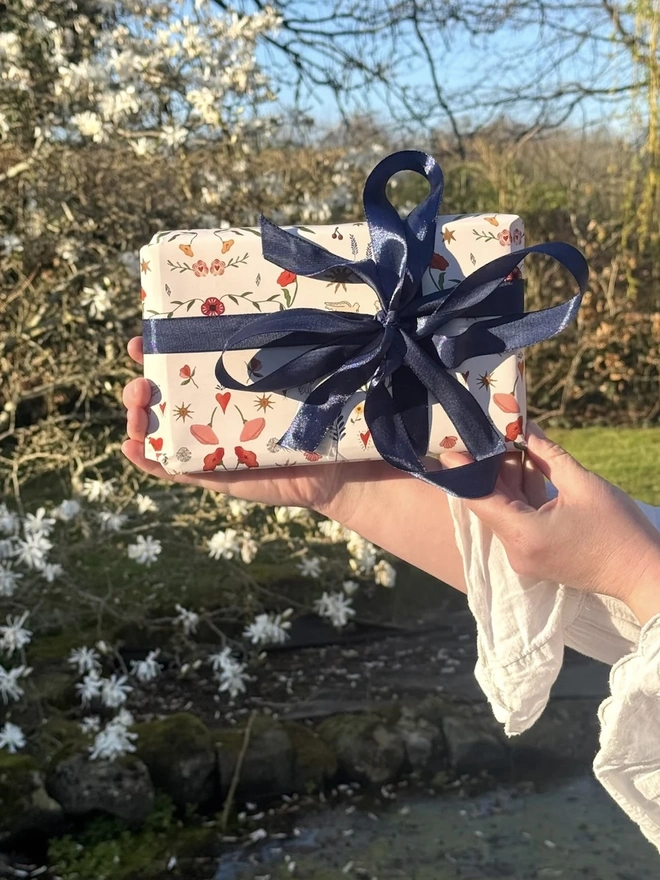 Folk Love Gift Wrap (3 Sheets), a person holding a present gift wrapped outside. 