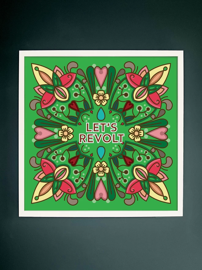 A symmetrical square design in greens, yellows and pinks with Let’s Revolt at the centre in a white frame hung on a dark grey wall.