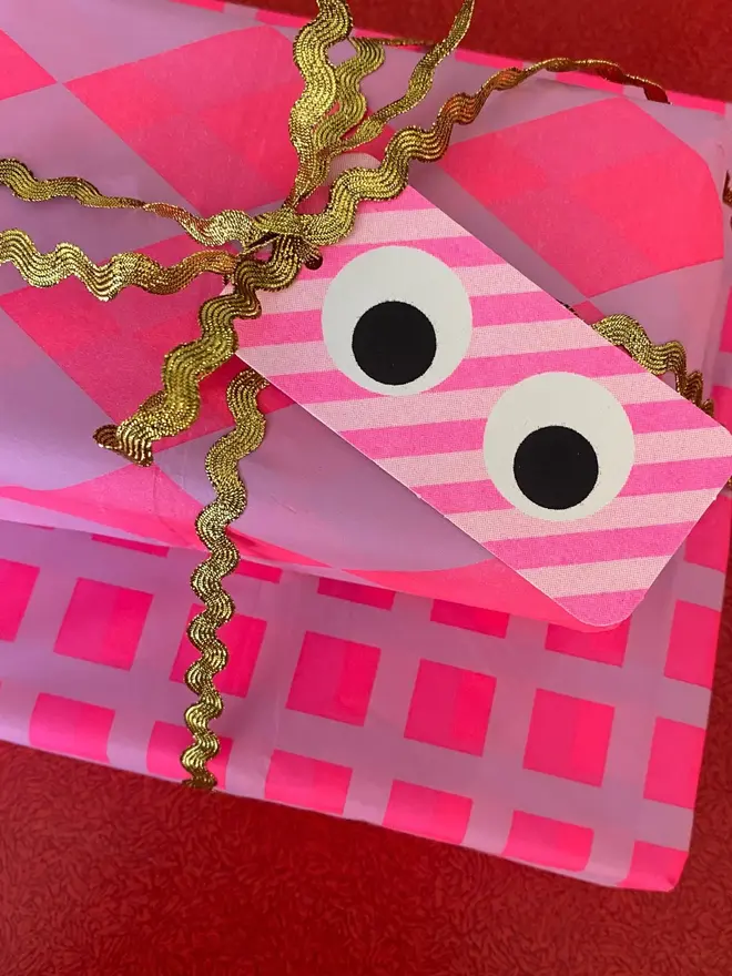 googly eye gift tags. a pink stripy gift tag on a gift wrapped in pink paper.
